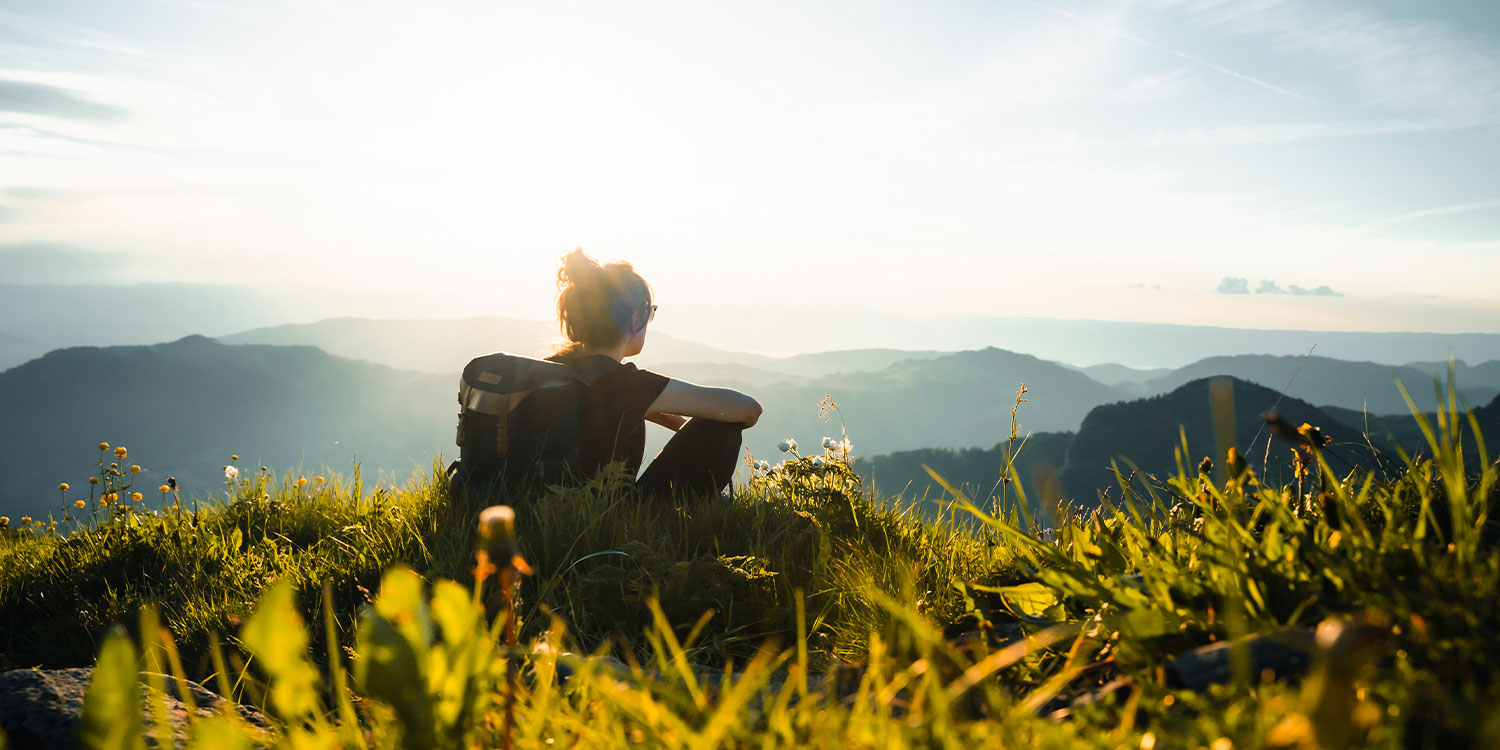 Photo d'une jeune femme assise dans l'herbe contemplant des montagnes au loin